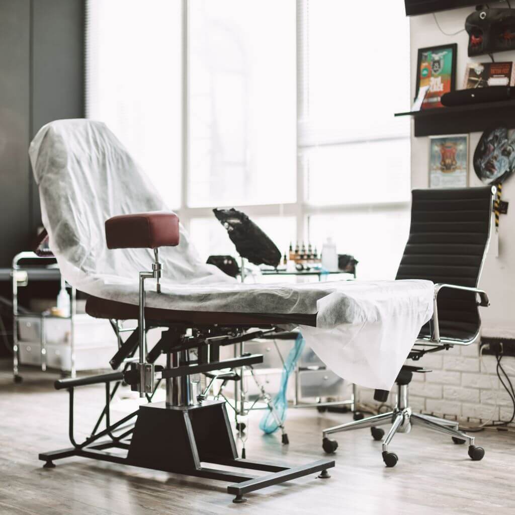 studio furniture with safety sheet over it and chair with tattoo needle and stool and armrest