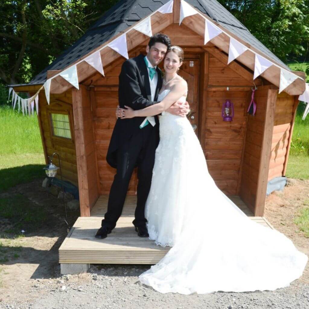bride and groom embracing in front of eco pod camping cabin with bunting 