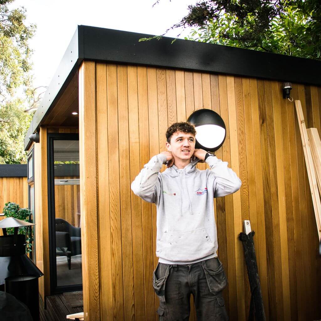 man in branded arctic cabins cabin master grey hoodie in front of cedar garden office at Nottingham Show Site