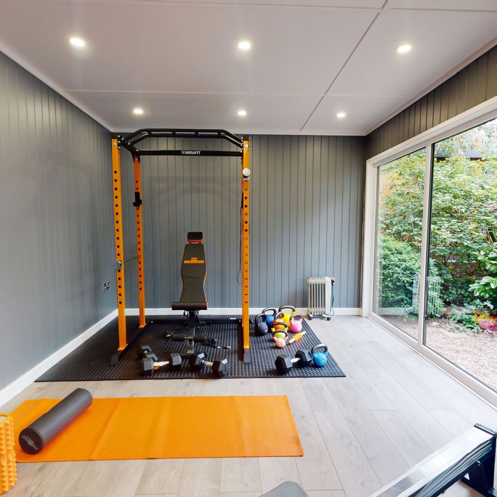 large glass doors inside garden gym building with large orange mat, body roller, squat rack and dumbbells