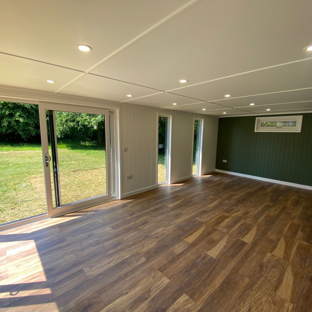 large garden room with click lock flooring and green feature wall with large sliding glass doors