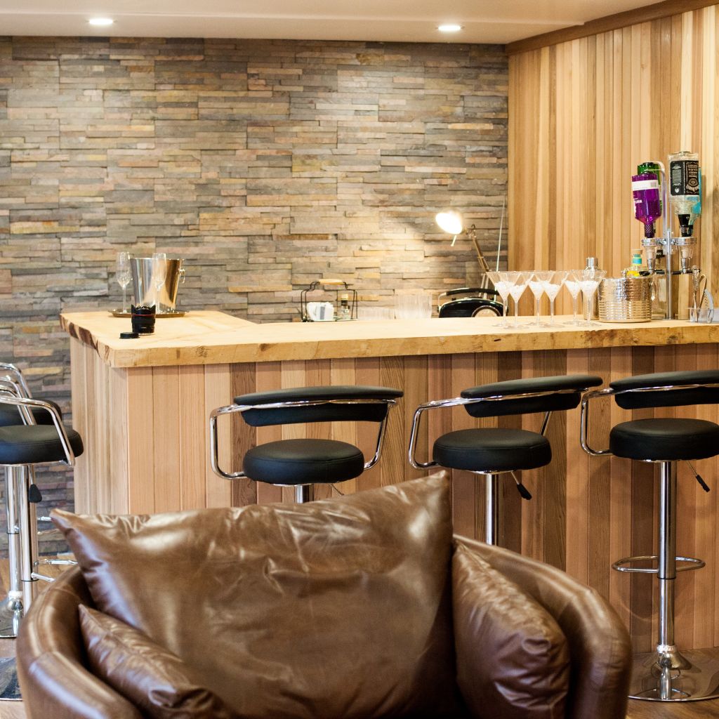 large garden bar with slate feature wall and black leather bar stools 