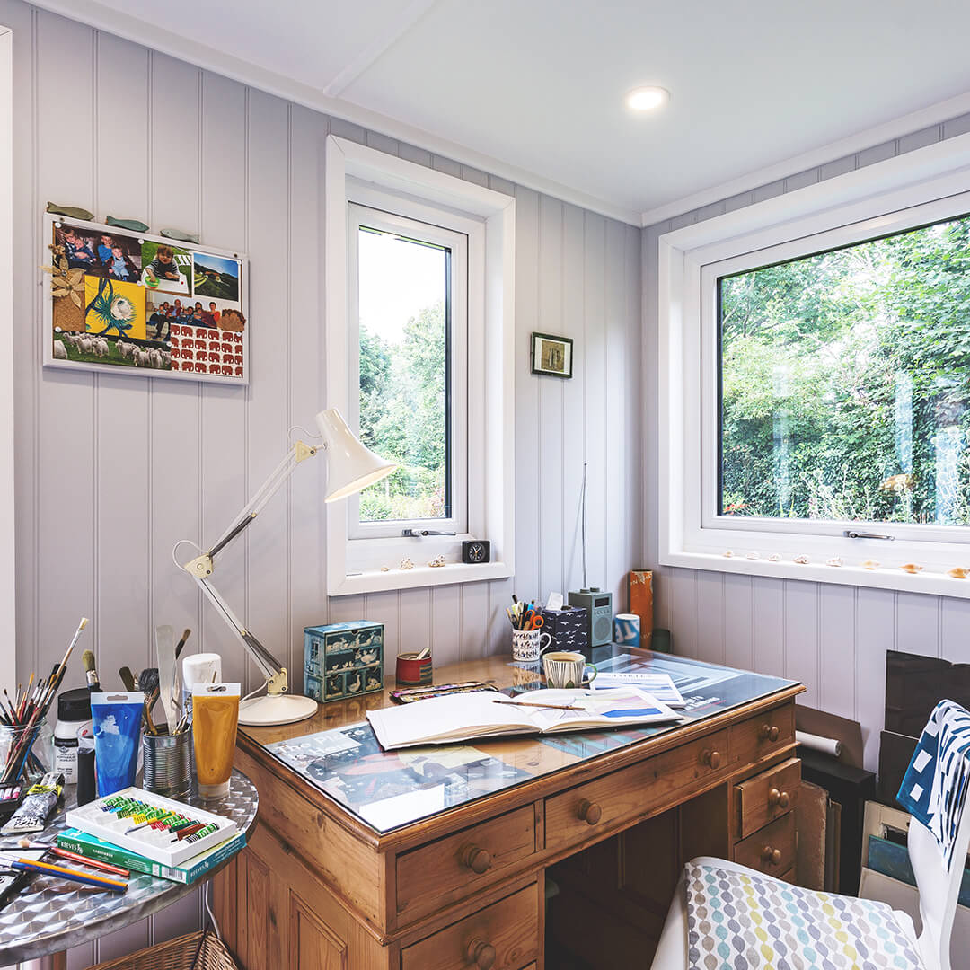 inside of hobby and craft room with large desk and paints and sketchbook with large glass windows