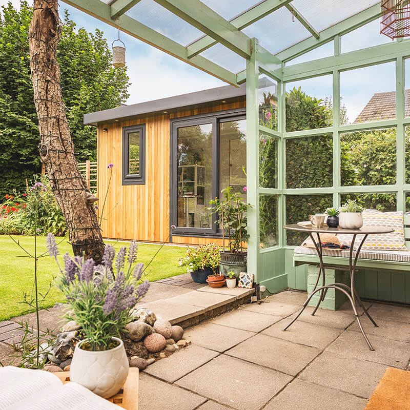 cedar garden room artists studio with green trellises and garden furniture and flowers and hedges