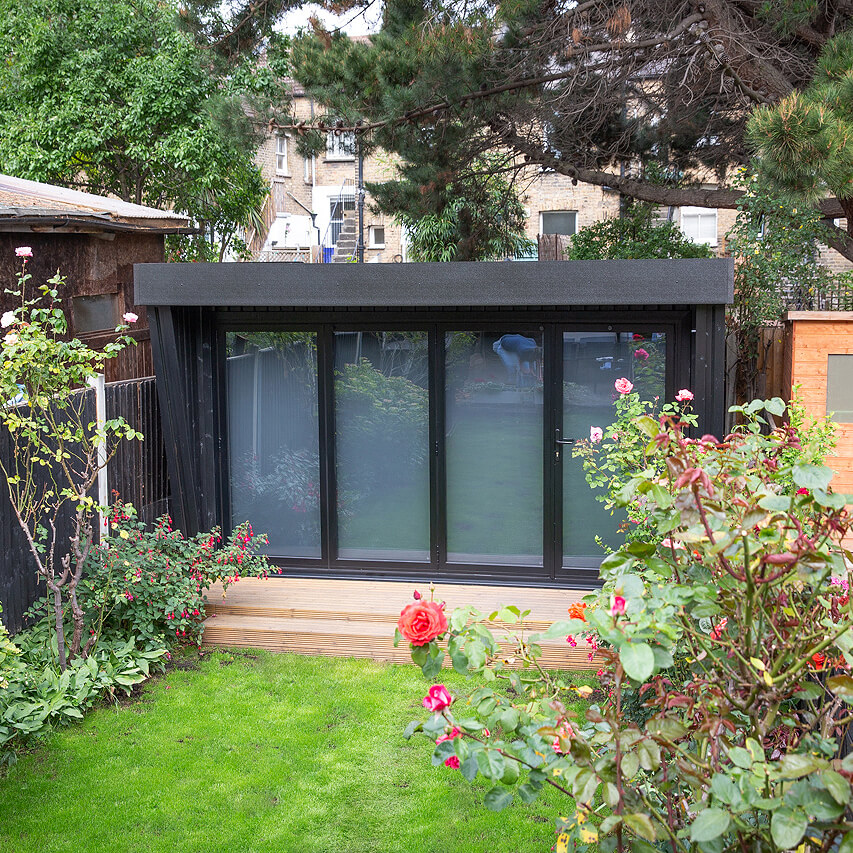 a garden area with a small black timber building in the middle of it