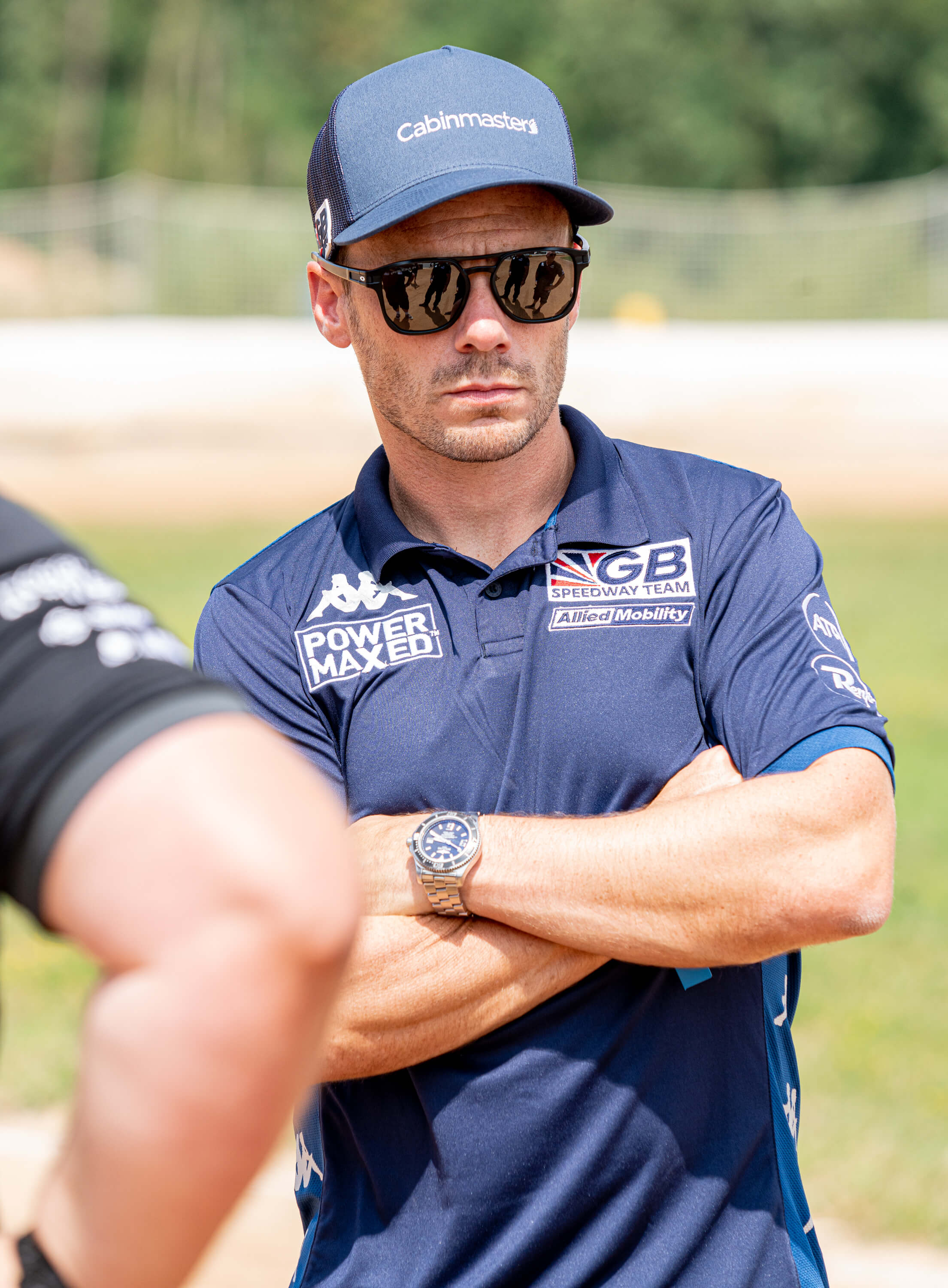 Man wearing Cabin Master Cap with black sunglasses and GB Speedway Polo T-shirt with arms crossed 