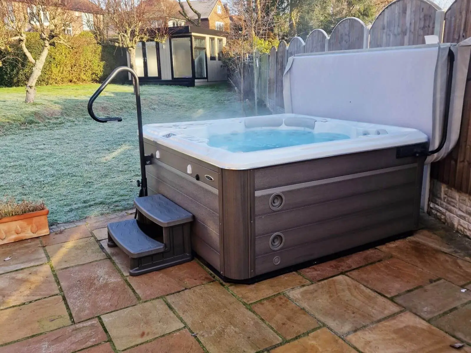 hydropool midlands hot tub in garden with grassy area with patio and step and cabin master garden room in background