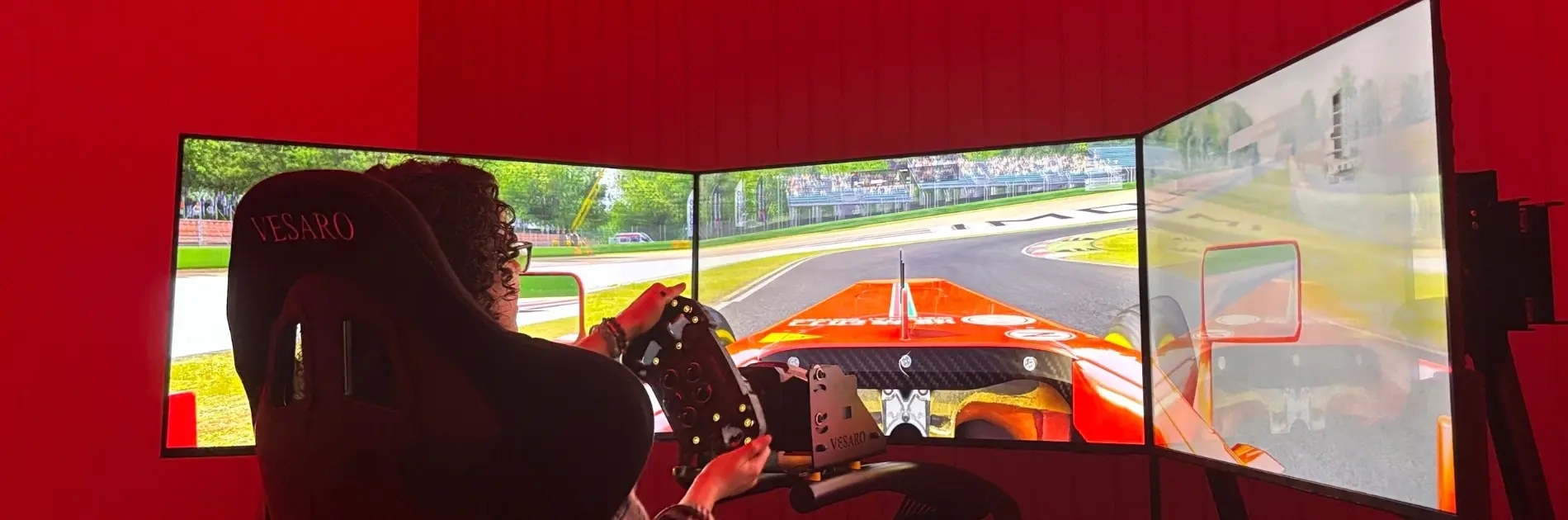 Driving simulator with three screens in a room lit with red strip lights
